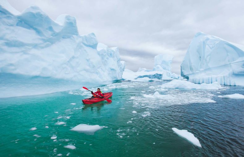 Man paddling on kayak between ice in Antarctica in Iceberg Graveyard, near Pleneau island